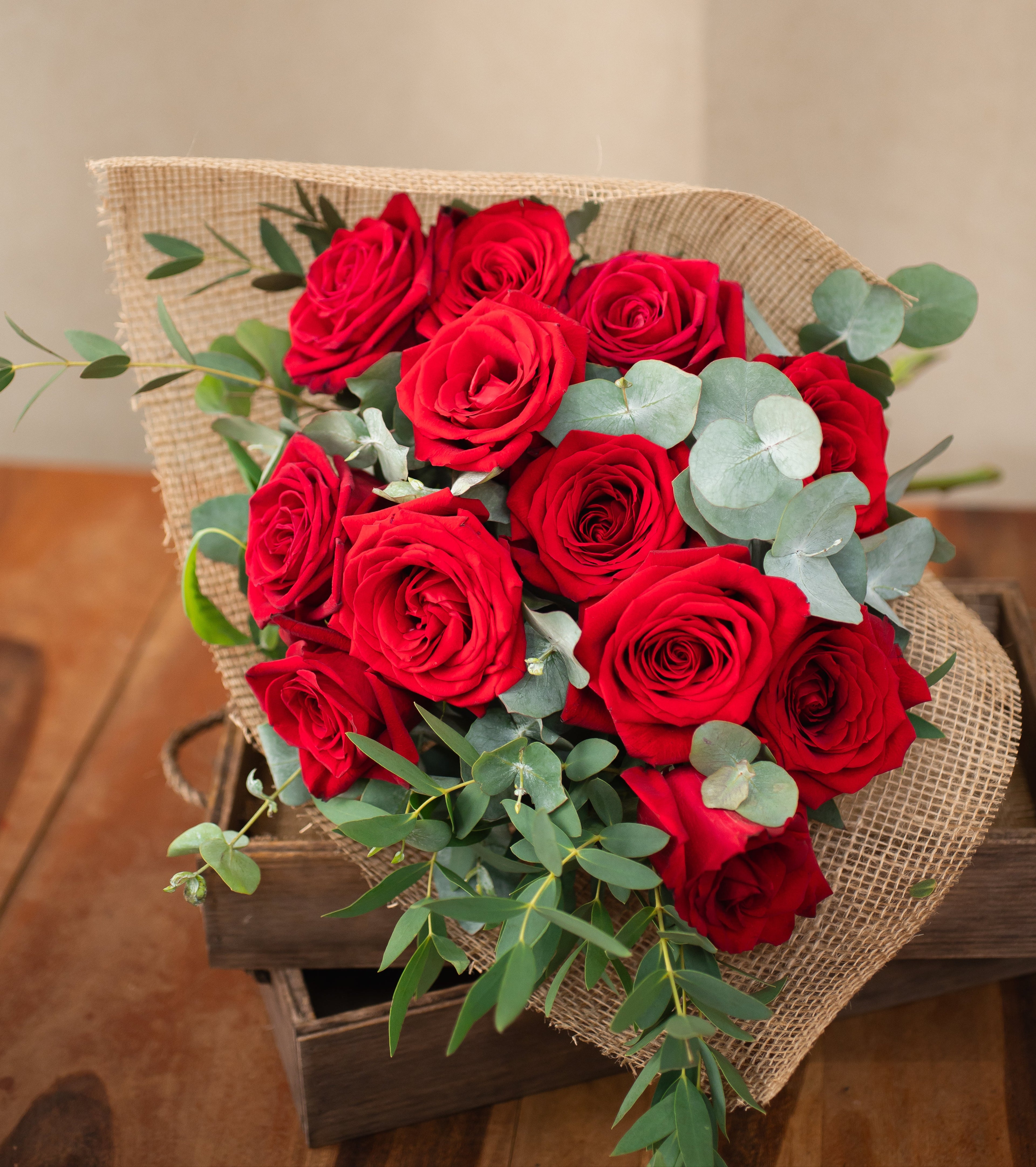 Bouquet of red roses with greenery on a wooden surface